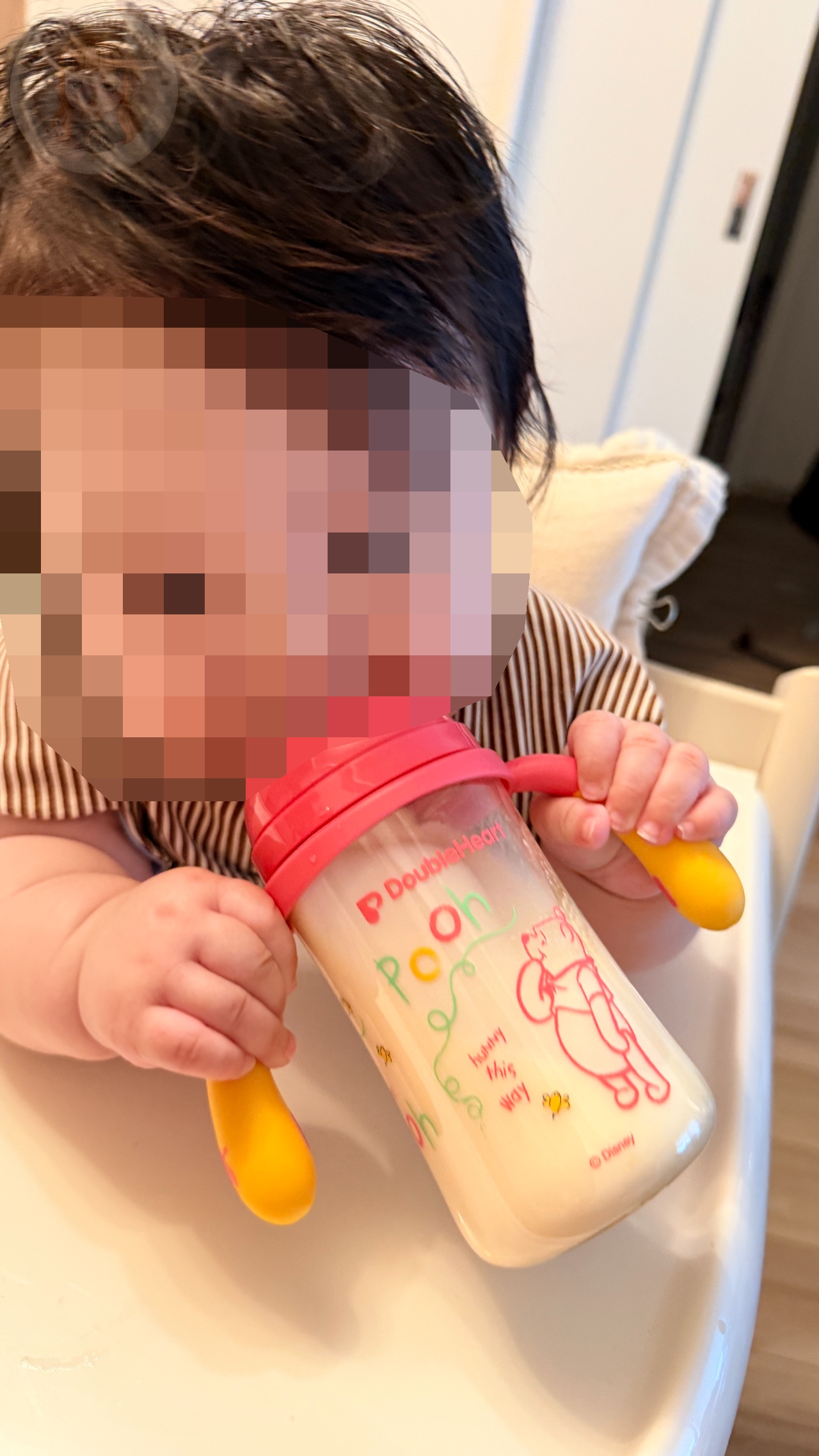 プーさん柄哺乳瓶の持ち手を両手で握る子ども。顔はプライバシー保護のためモザイク加工